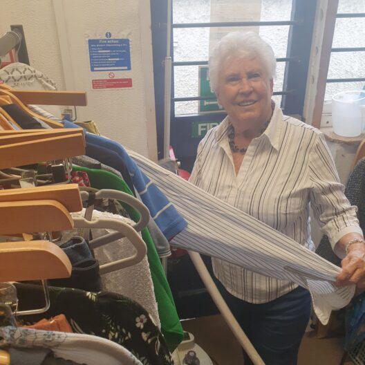 A lady holds the sleeve of a shirt in one hand and a steamer in the other