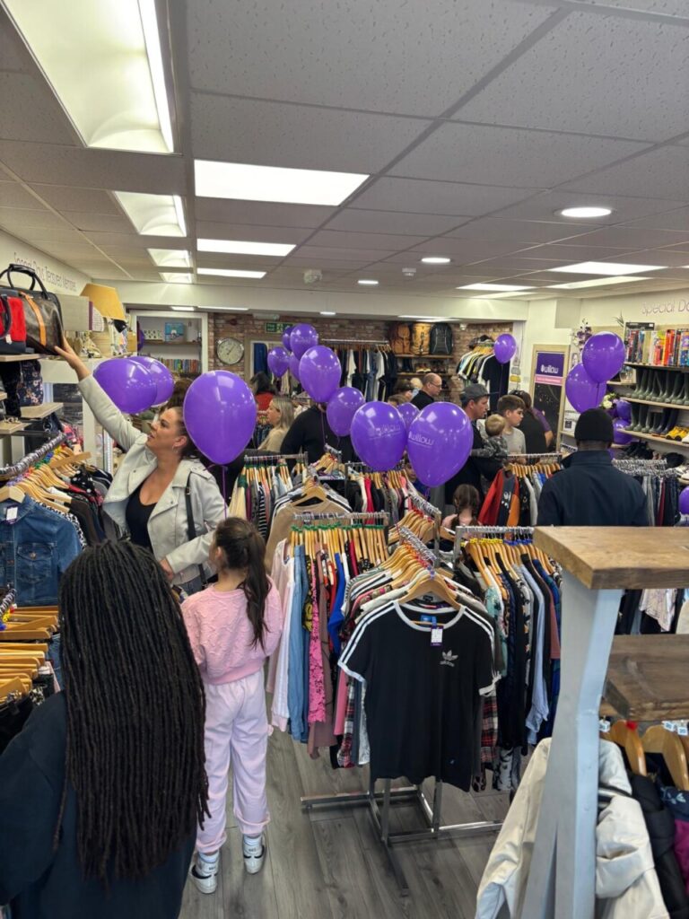 Inside Willow charity shop in Stevenage where there are purple balloons attached to all the clothing rails. 