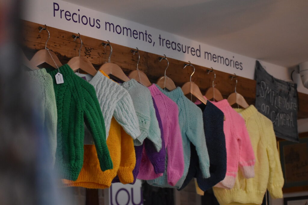 A line of children's jumpers inside Willow Biggleswade shop, wall stickers above read "Precious moments, treasured memories" 