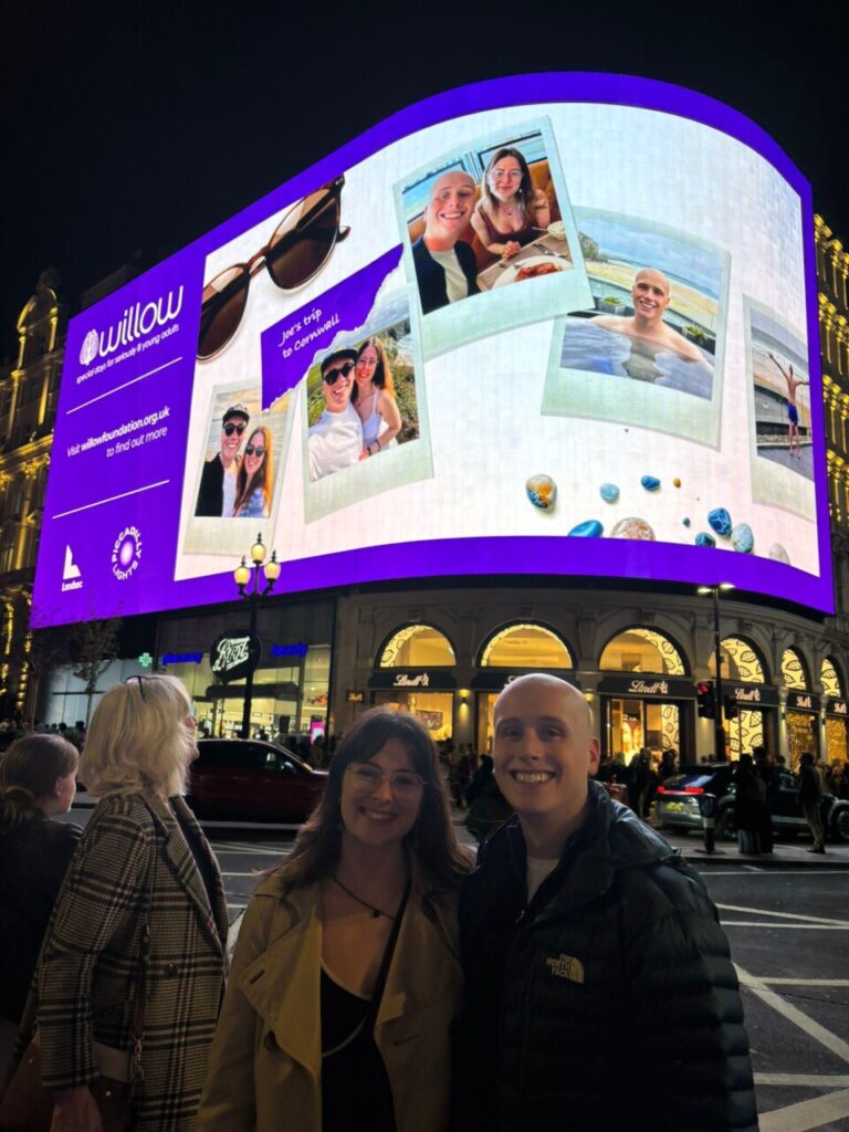 Joe and his wife in front of their feature on the Piccadilly Lights in London