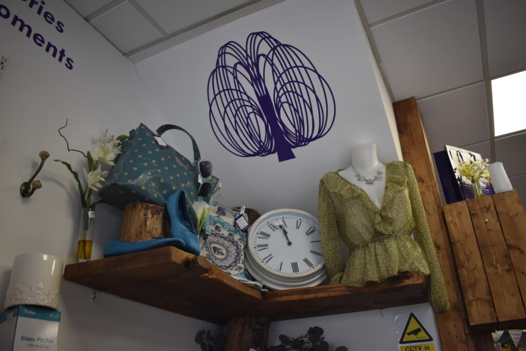 Willow logo above wooden shelf hosting items for sale at Willow charity shop Hertford. 
