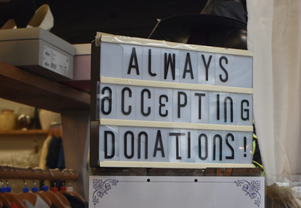 Sign reads "always accepting donations" and sits in Willow's Hitchin Charity shop window