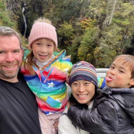 A young family - a man, a woman, and their two children, smiling at the camera on a break in the Scottish Highlands, arranged by Willow Foundation