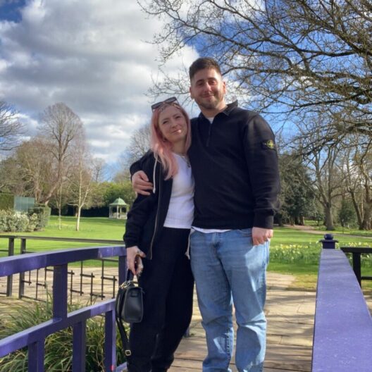 Laura and Jake standing together in Sopwell grounds, with a sunny blue sky behind them.